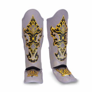 Paire de protège-tibias TopKing modèle Kanok, gris avec motifs dorés inspirés de l’art traditionnel thaïlandais. Design incurvé avec rembourrage et sangles pour un maintien optimal, adaptés aux sports de combat comme le Muay Thai ou le kickboxing.