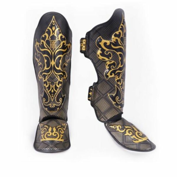 Paire de protège-tibias TopKing modèle Kanok, noirs avec motifs dorés inspirés de l’art traditionnel thaïlandais. Design incurvé avec rembourrage et sangles pour un maintien optimal, adaptés aux sports de combat comme le Muay Thai ou le kickboxing.
