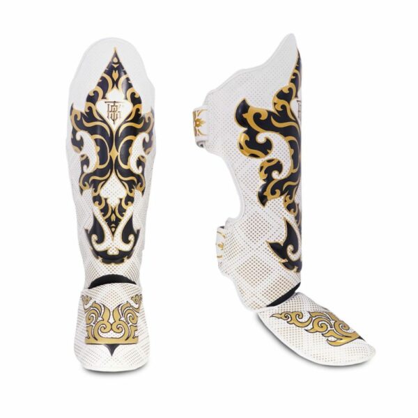 Paire de protège-tibias TopKing modèle Kanok, blanc avec motifs dorés inspirés de l’art traditionnel thaïlandais. Design incurvé avec rembourrage et sangles pour un maintien optimal, adaptés aux sports de combat comme le Muay Thai ou le kickboxing.